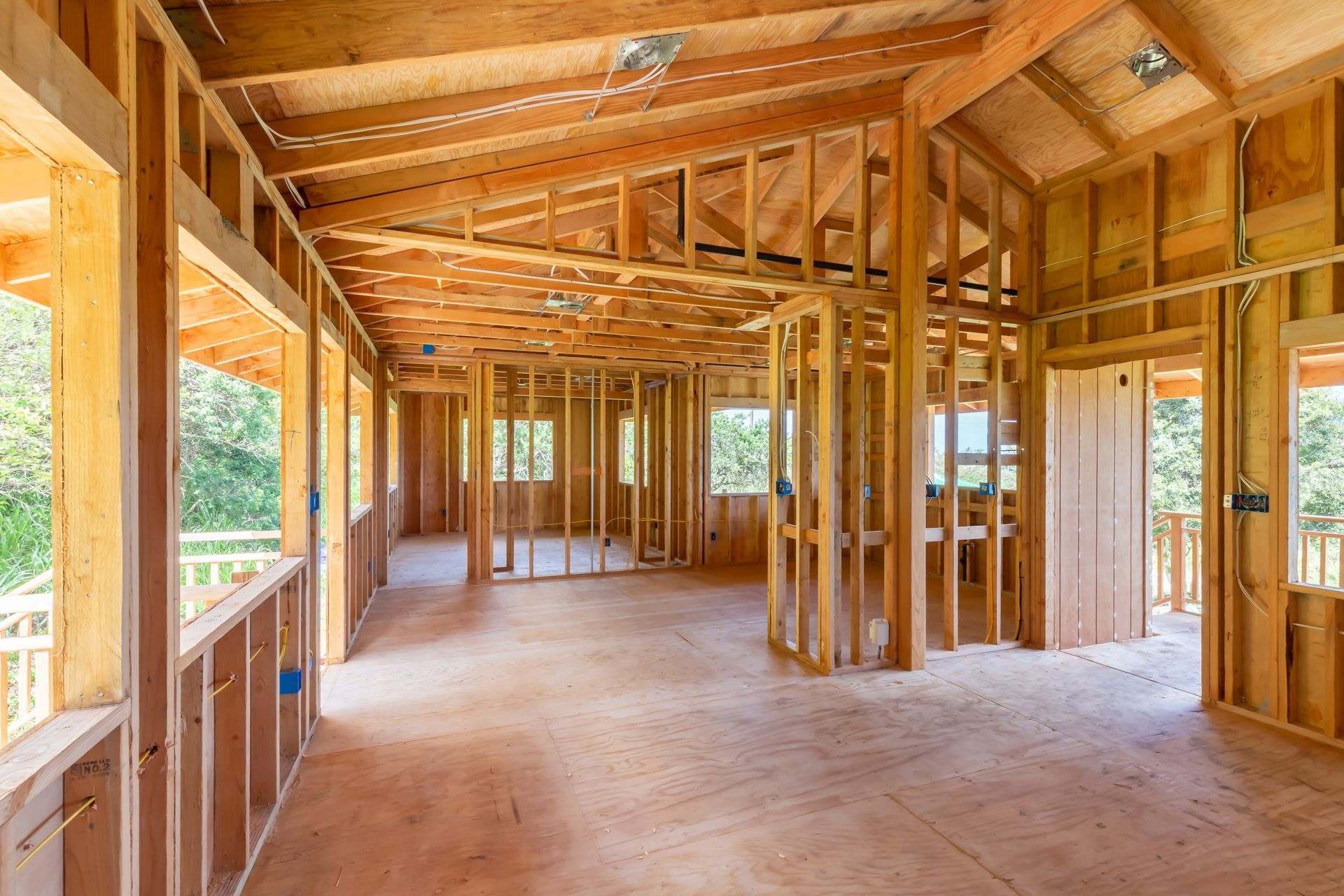 The inside of a house under construction with wooden beams and windows.