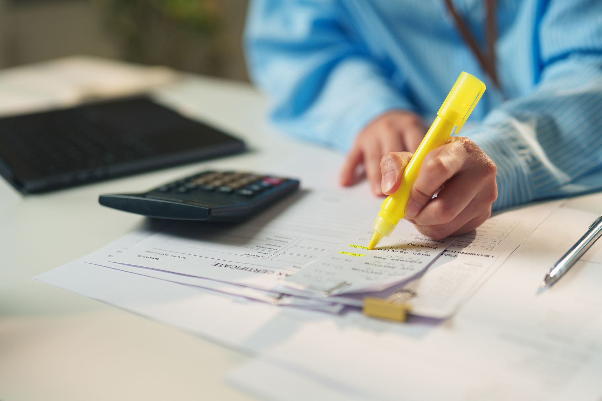 A woman uses a yellow highlighter on paper, with a calculator placed beside her on the table