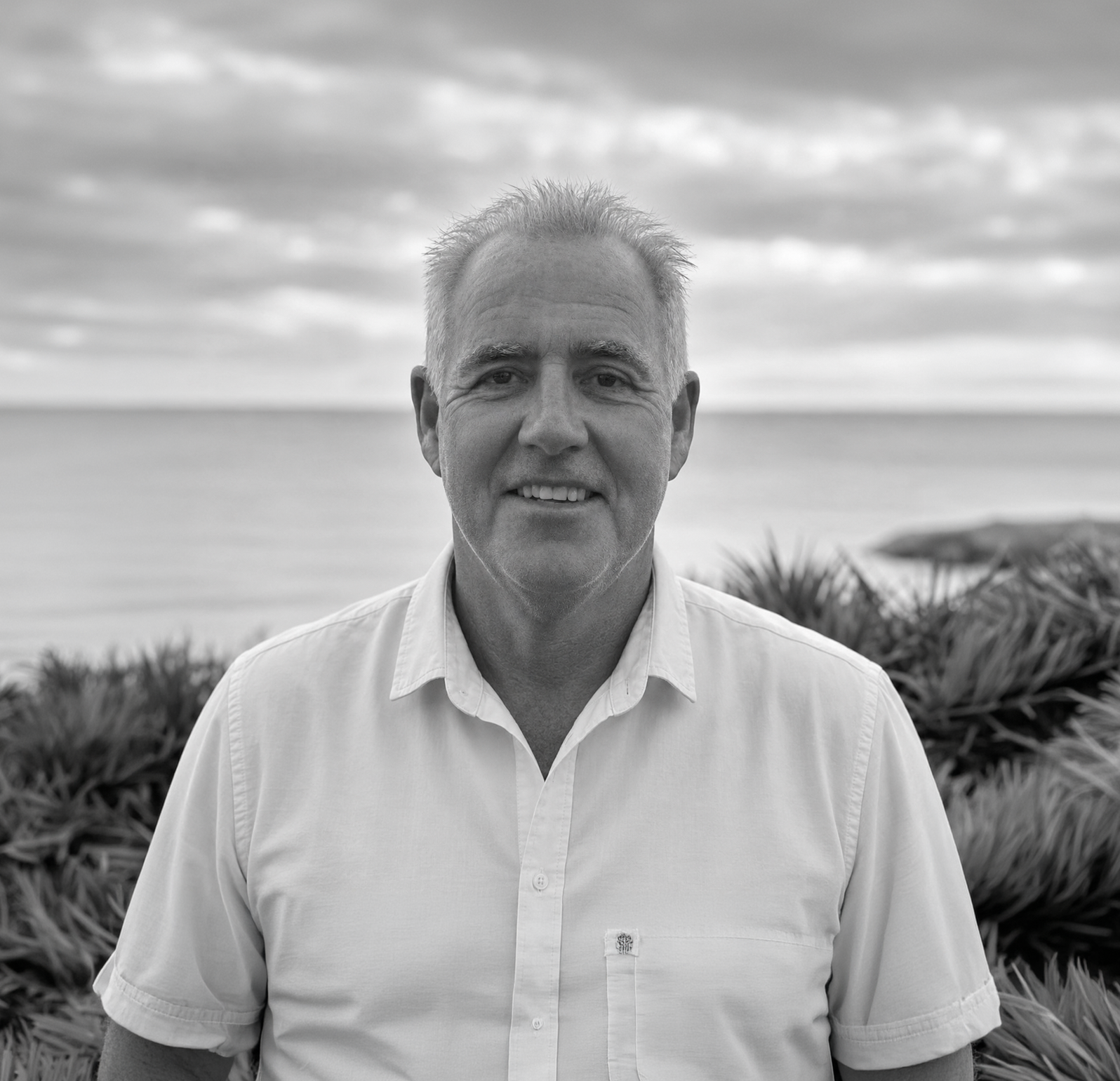 Mark (man) in a white shirt standing outdoors by the ocean