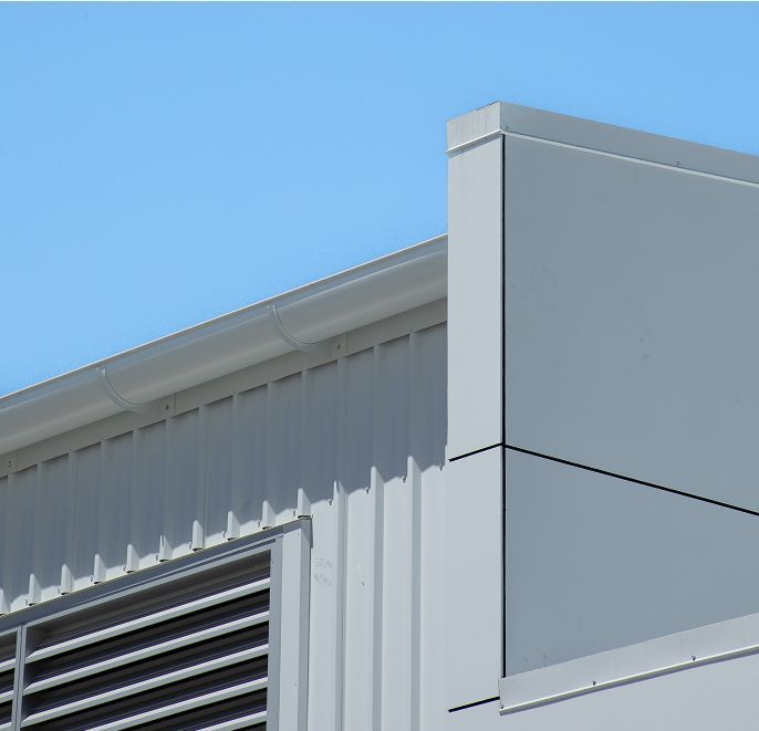 Exterior of a white industrial building corner with vents against a clear blue sky
