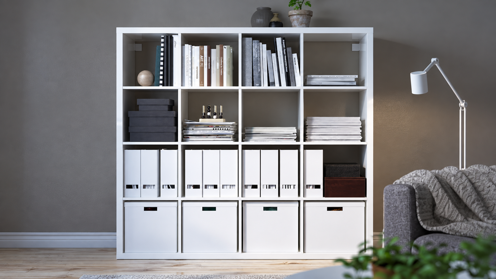 White cube bookshelf with boxes and books in a gray living room beside a floor lamp and sofa