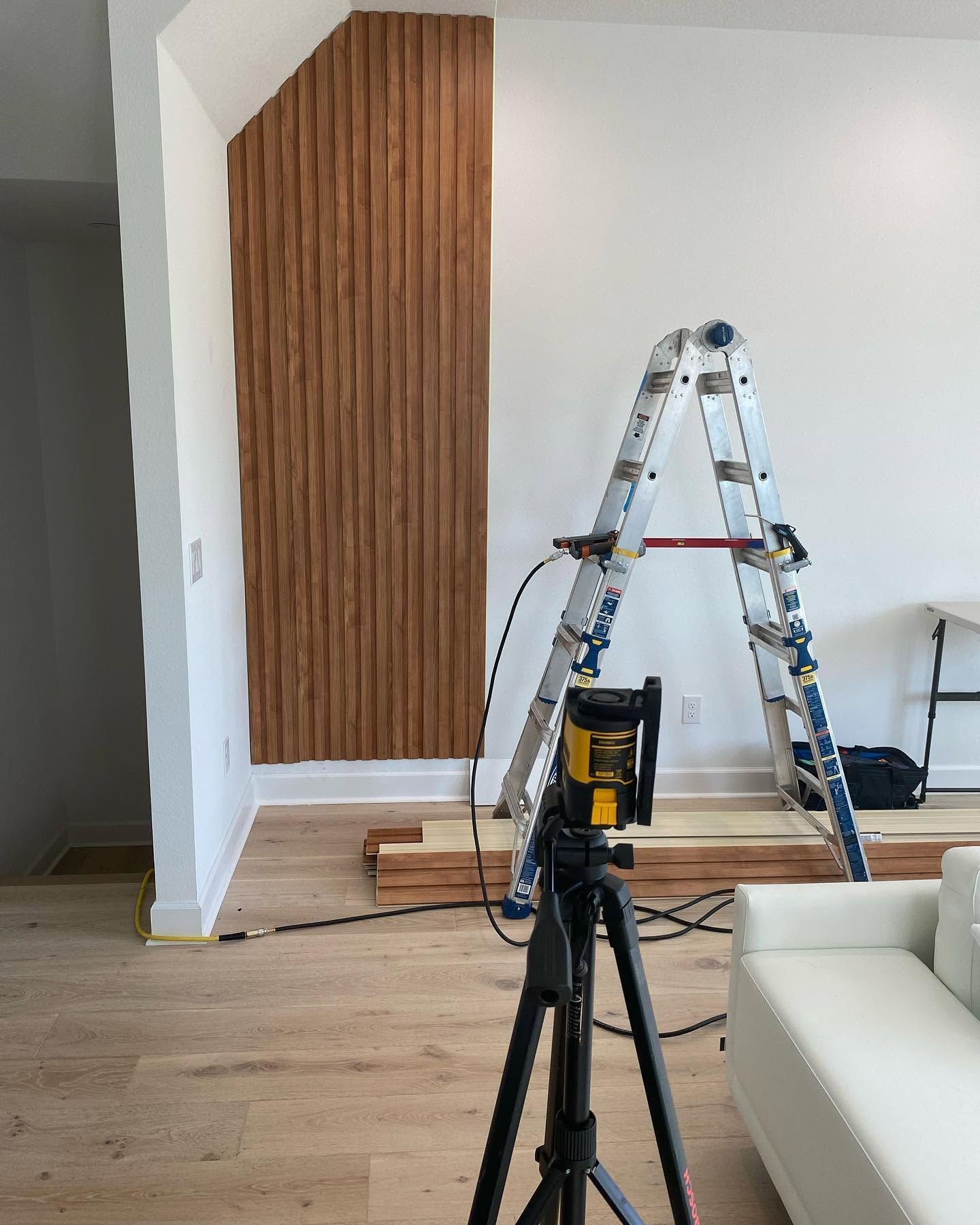 Living room with ladder, tripod, and tools during interior wall renovation