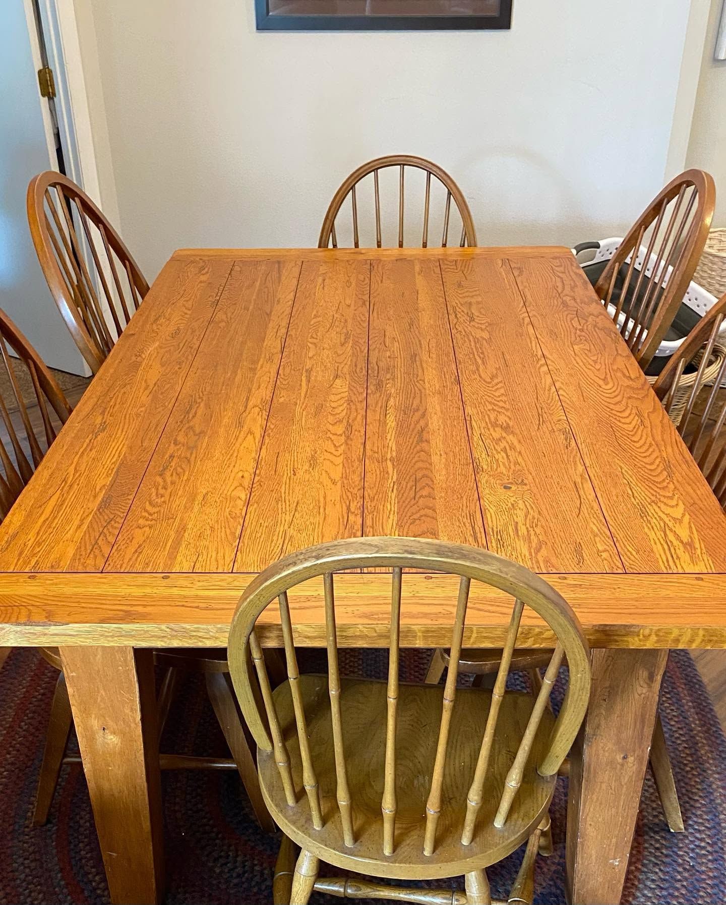 Wooden dining table surrounded by six chairs in a plain dining room.