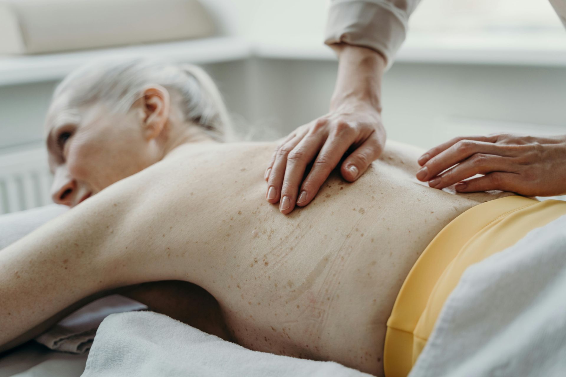Back massage, person lying prone on a table, another person's hands on their back. Yellow shorts.