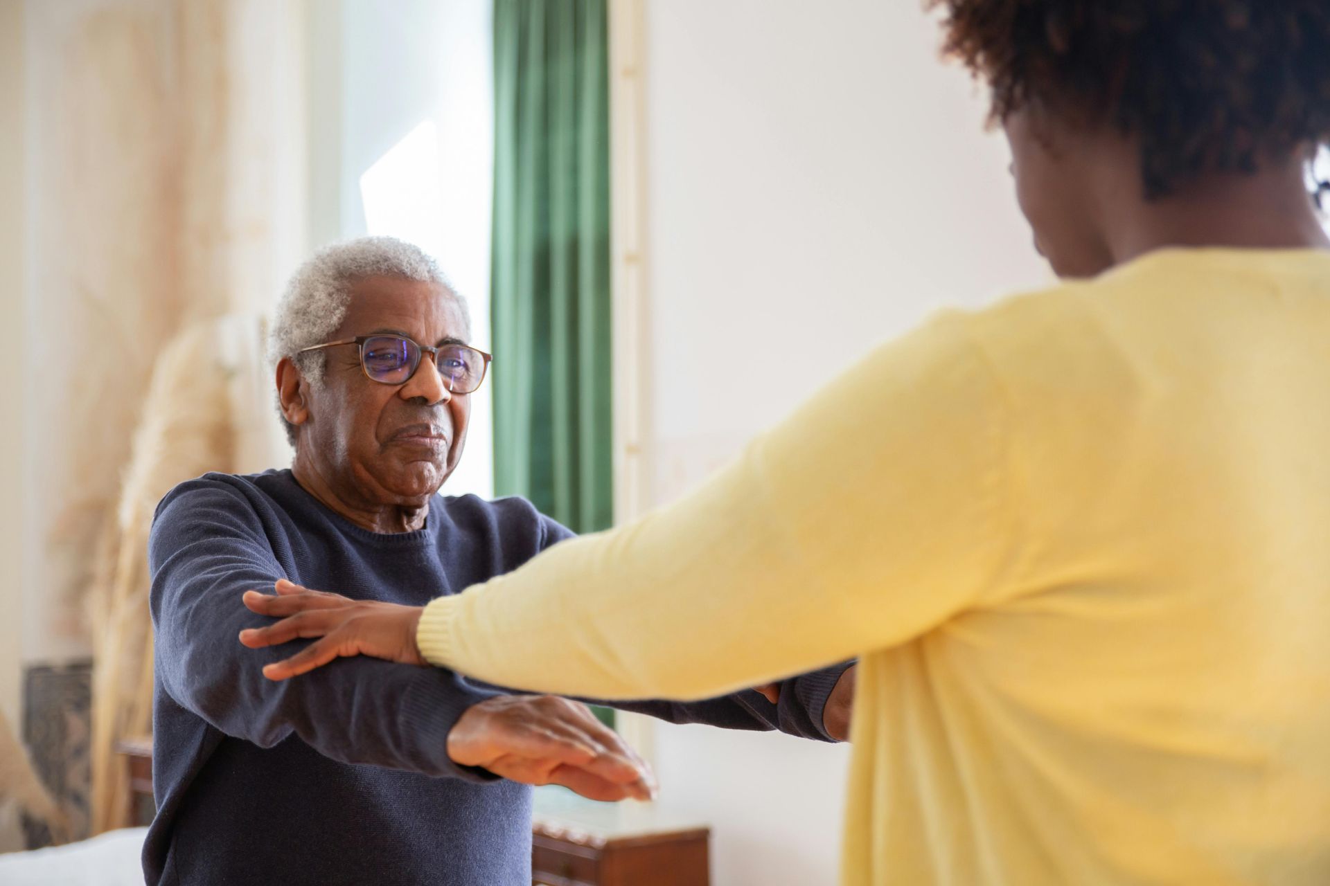 Older adult stretches arms with assistance from another person.