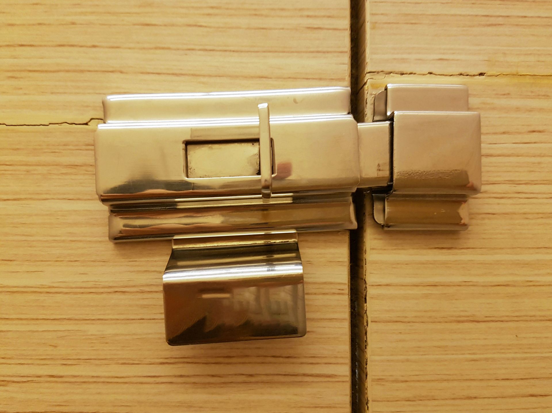 Close-up of a shiny metal door latch on a light wood cabinet door.