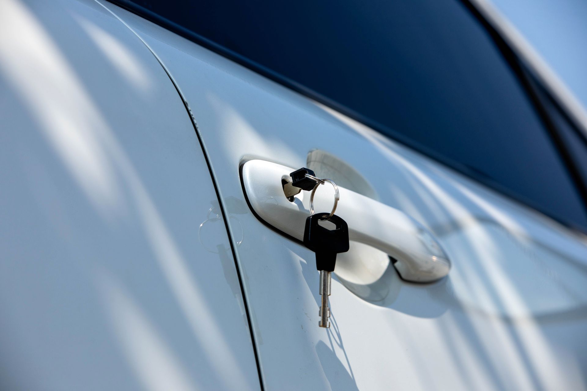 Keys in a white car door lock with the handle visible, in bright sunlight