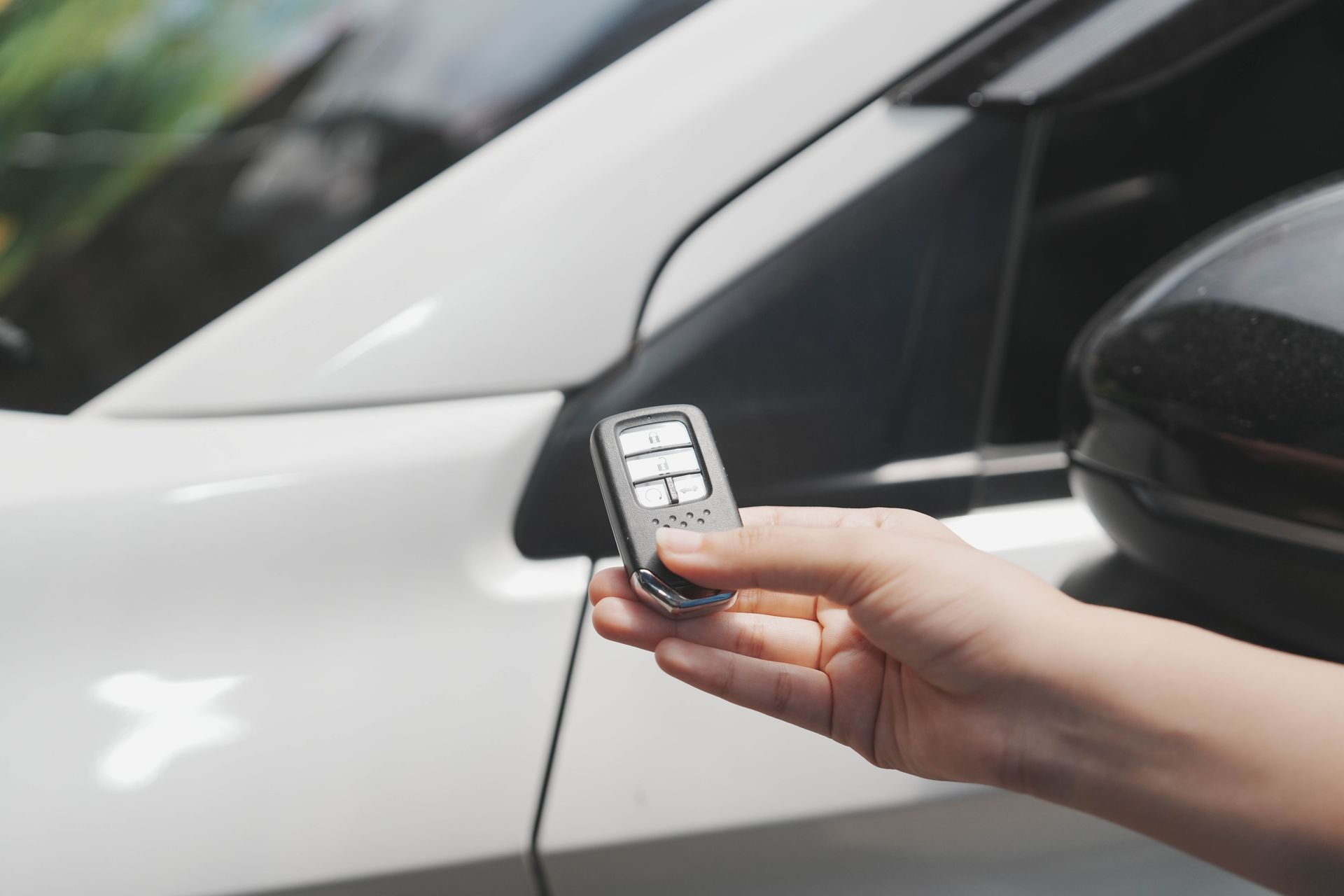 Hand holding a car key fob beside a white car door