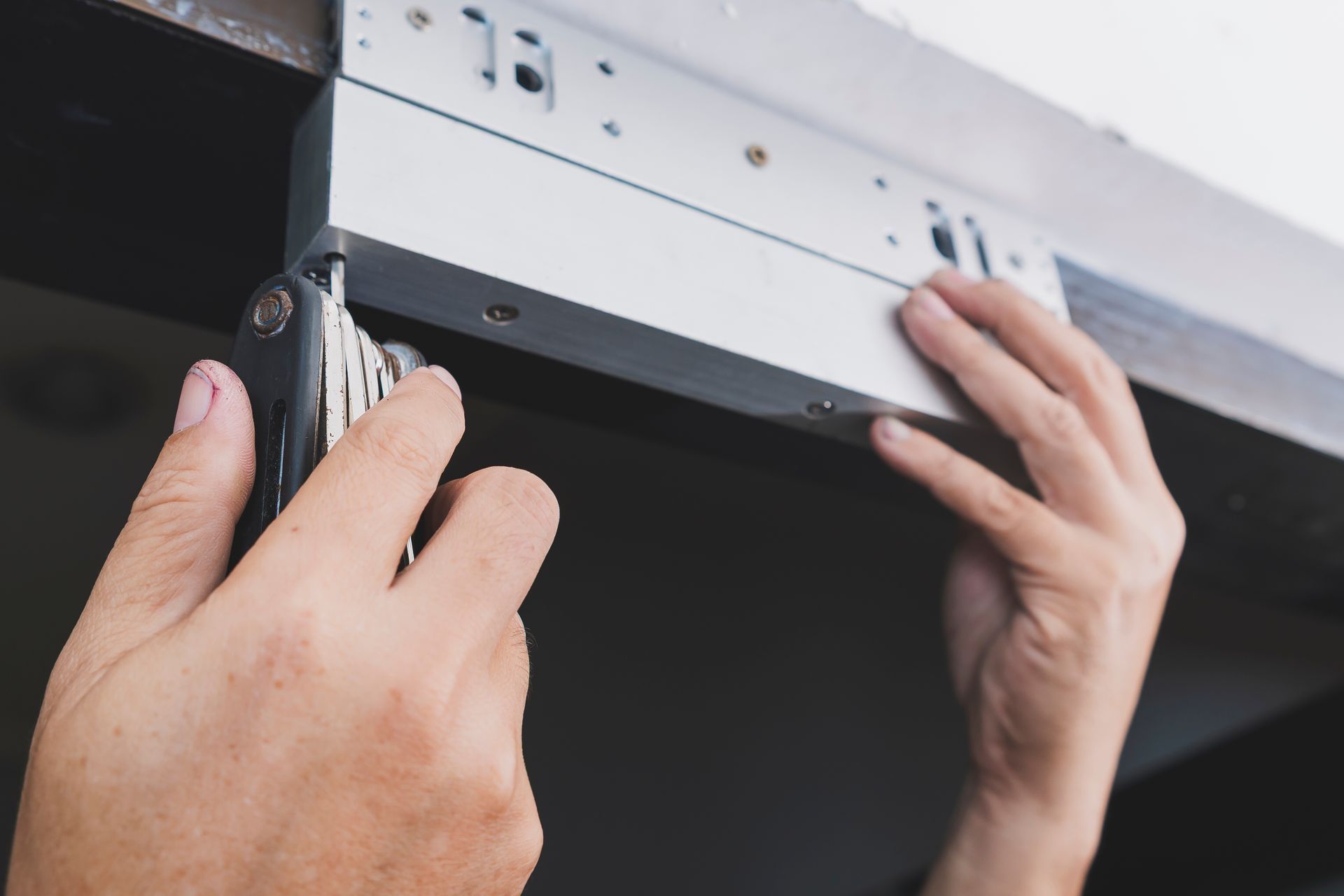 Hands installing a metal cabinet under a shelf with a screwdriver