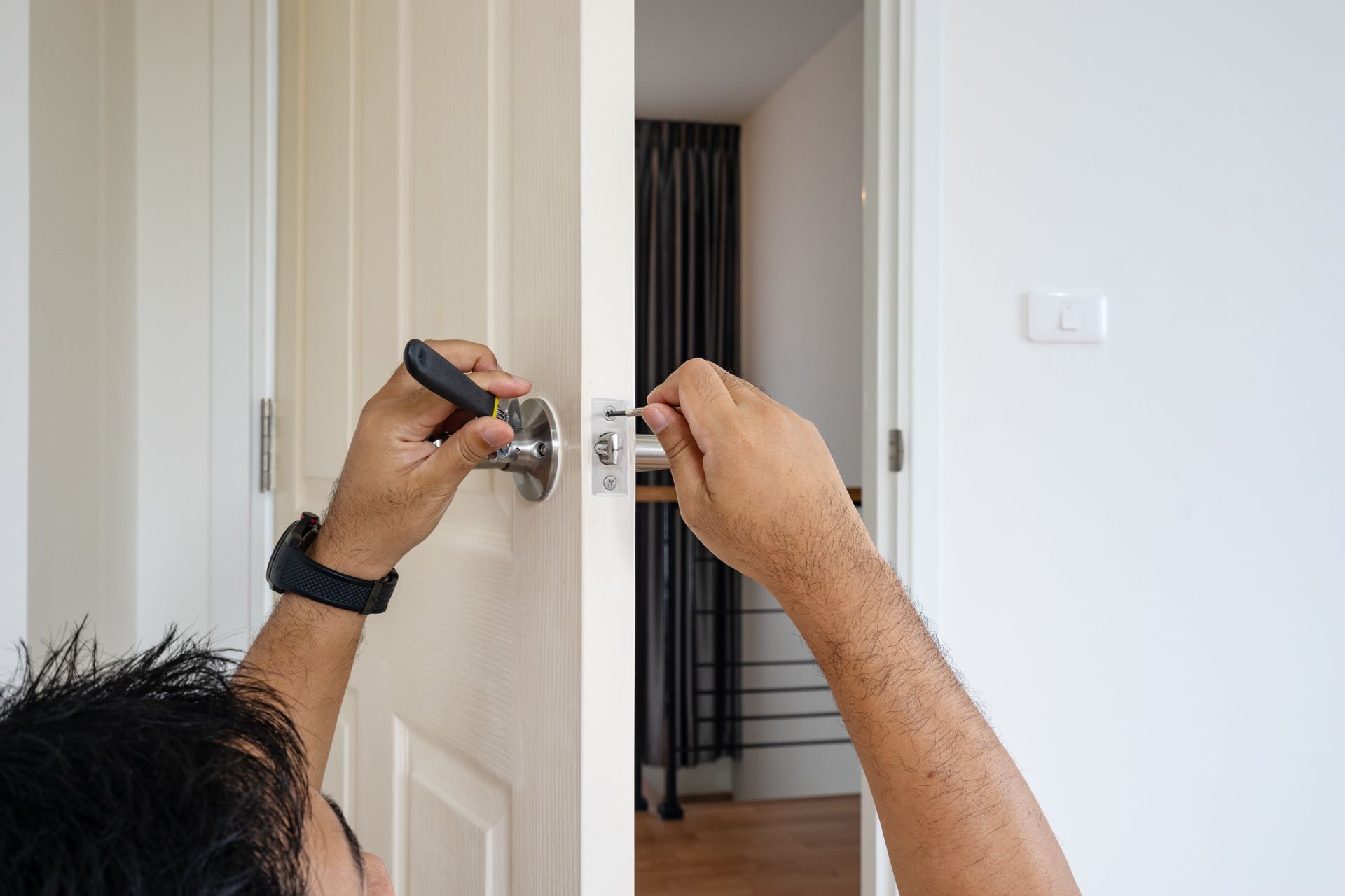 Hands using a screwdriver to install or repair a white door lock in a doorway