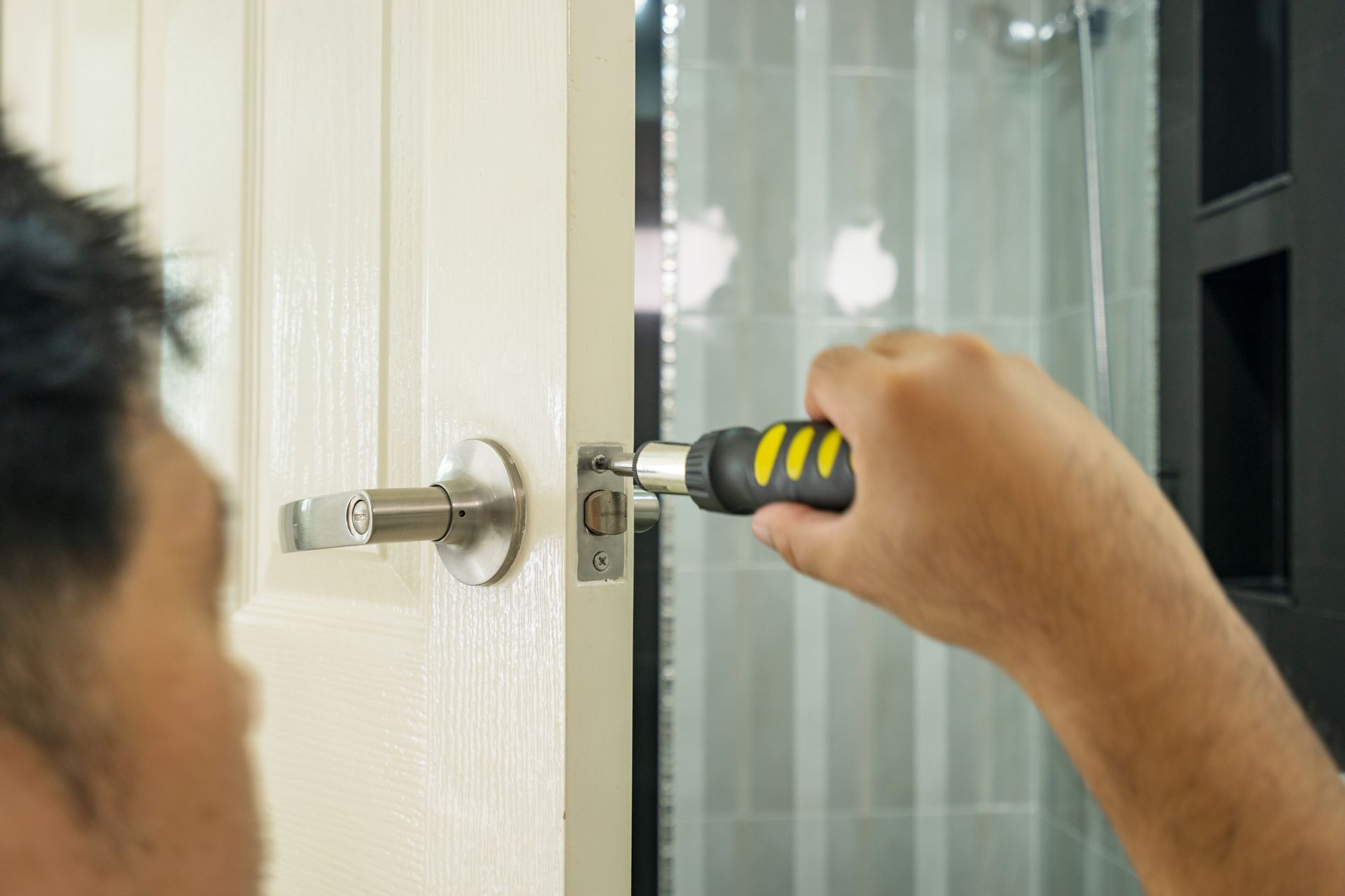 Person using a screwdriver to remove a door lock latch from a white door