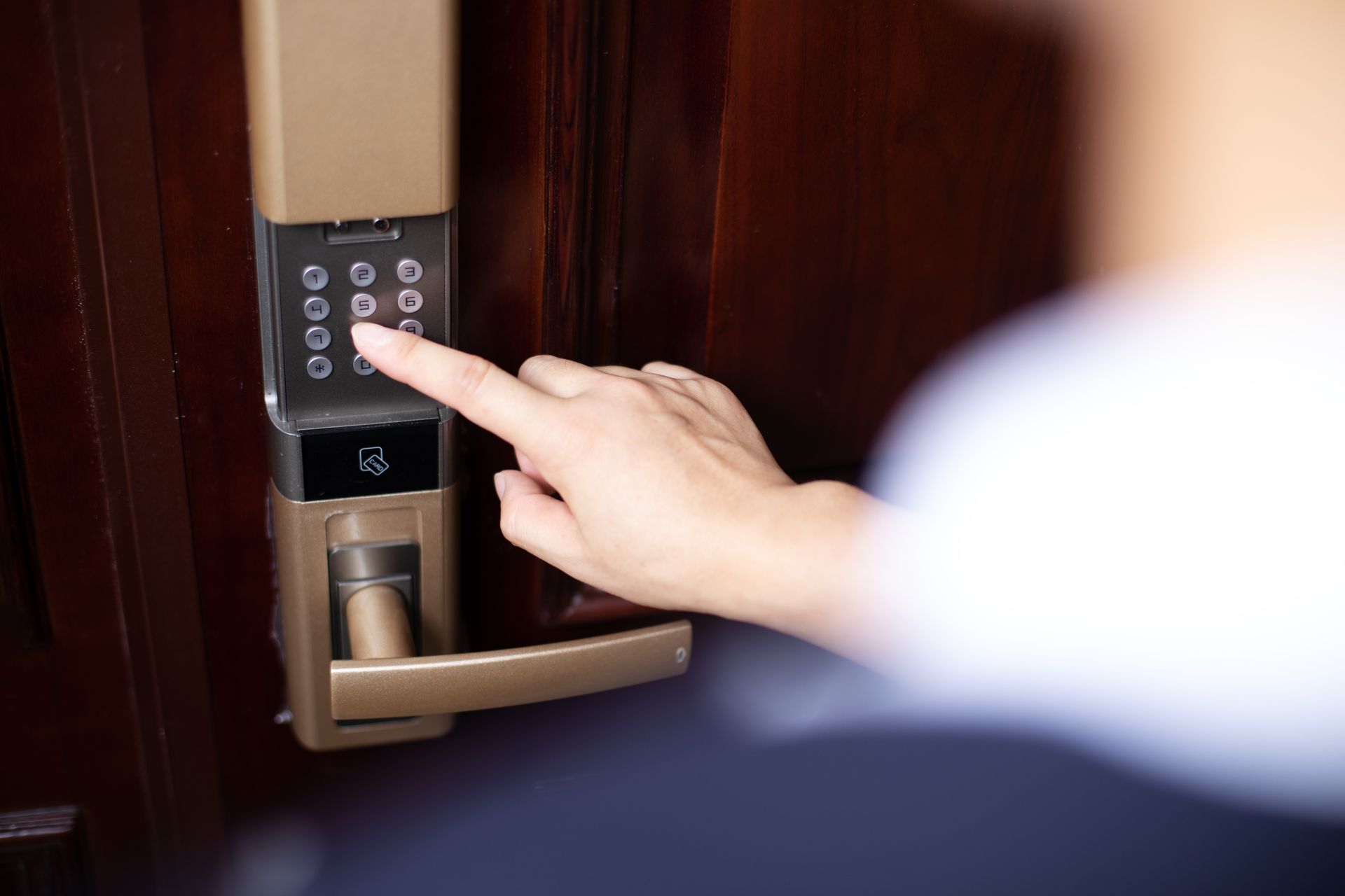 Hand entering a code on a black door keypad near a silver handle