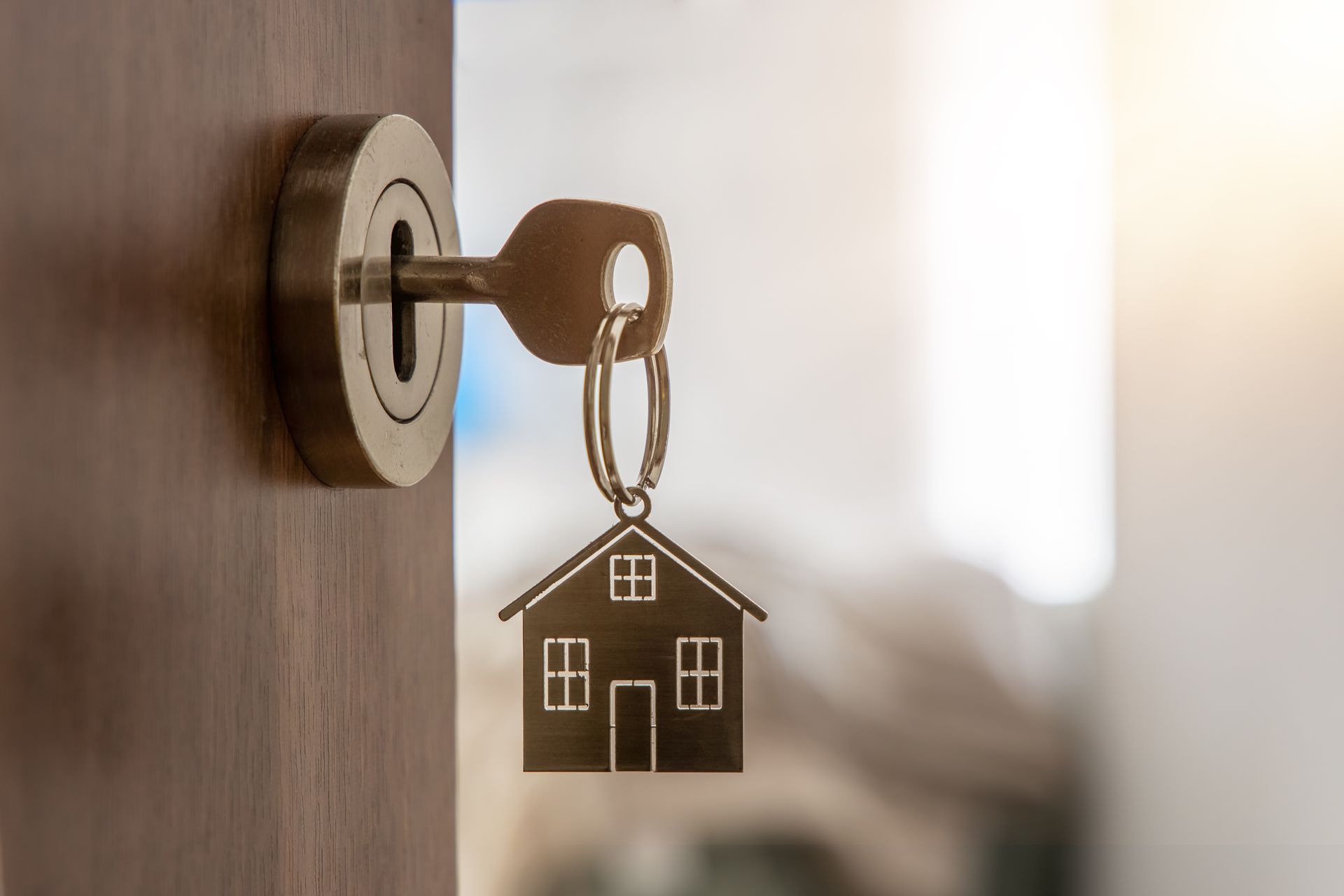 Key in a lock with a house-shaped keychain hanging from it on a wooden door