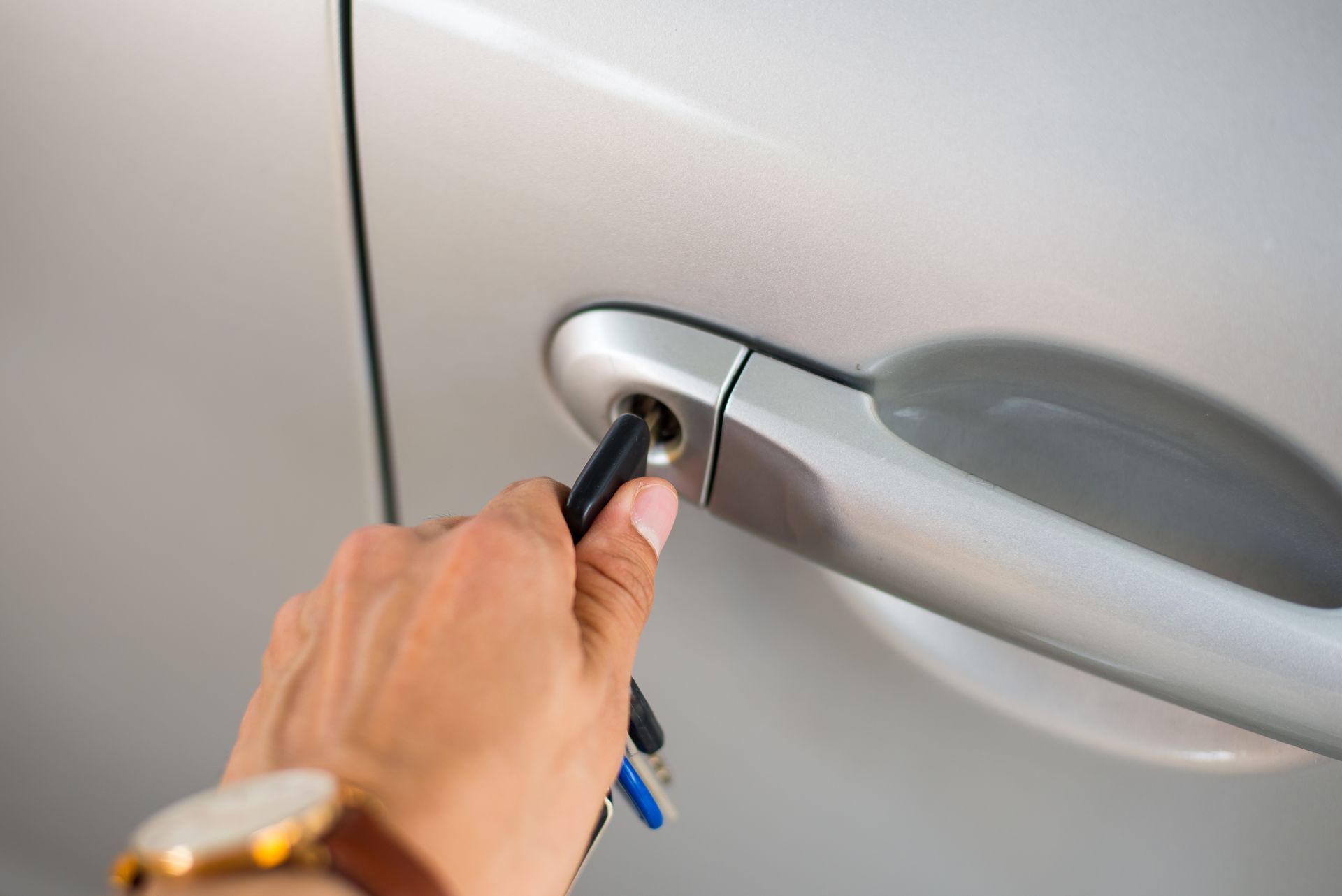Hand holding a car key near a silver car door handle, unlocking the vehicle