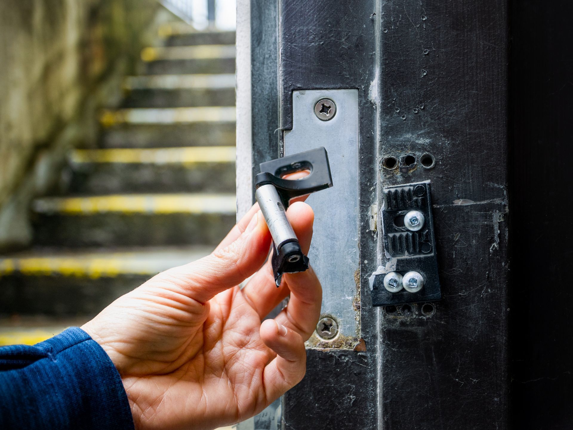 Hand inserting a black key into a metal door lock on a weathered doorway