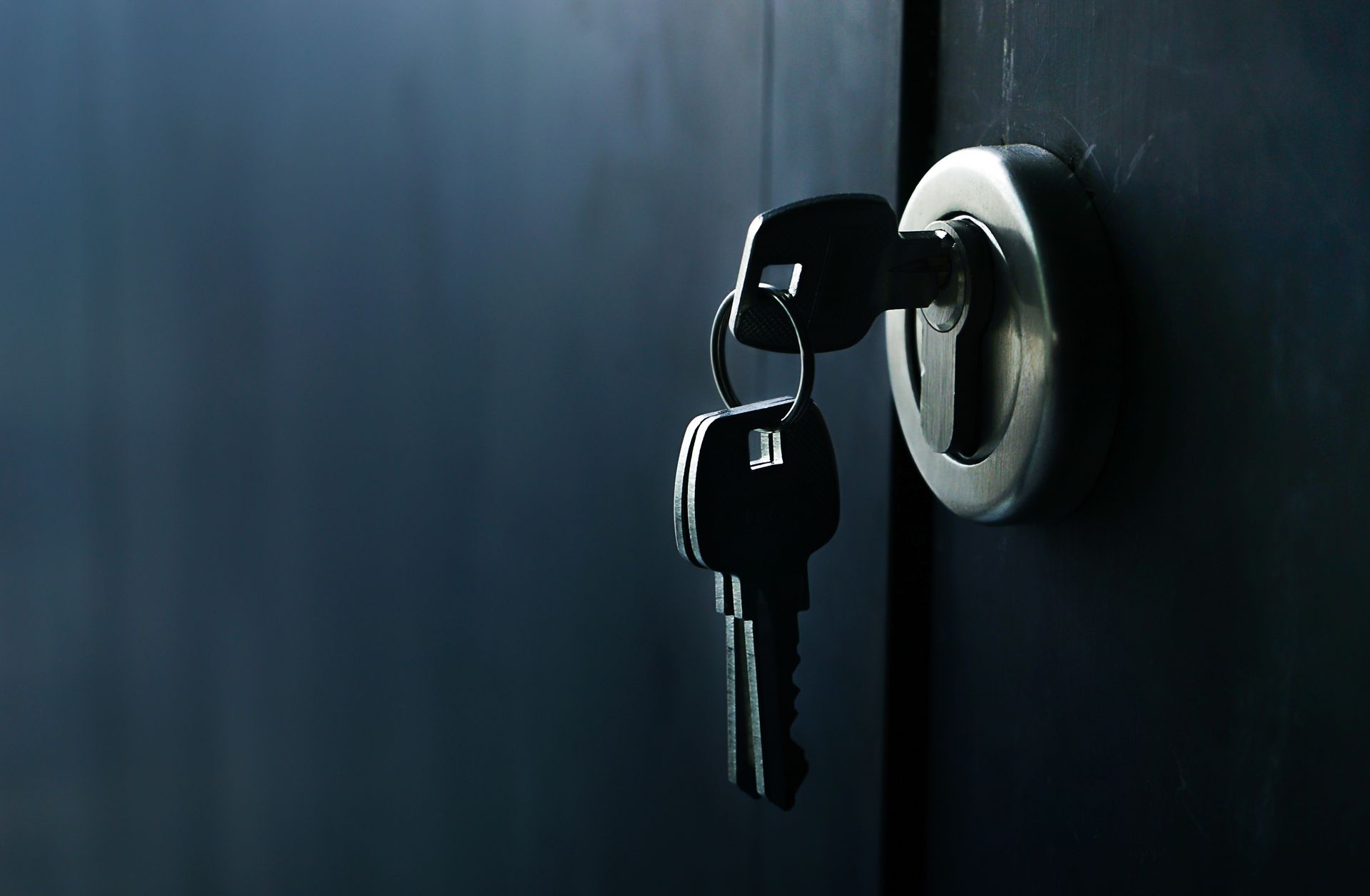 Keys inserted in a silver door lock on a dark blue door.