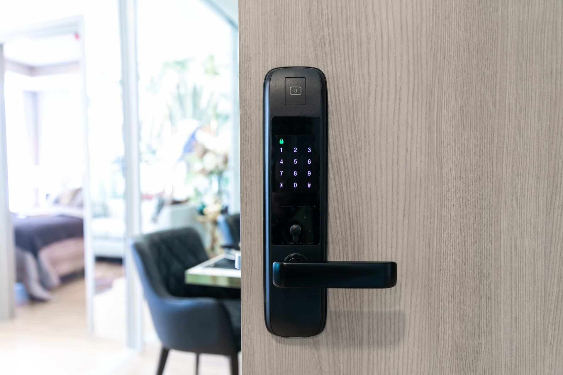 Modern black electronic door lock on a wooden door, with a blurred room visible in the background