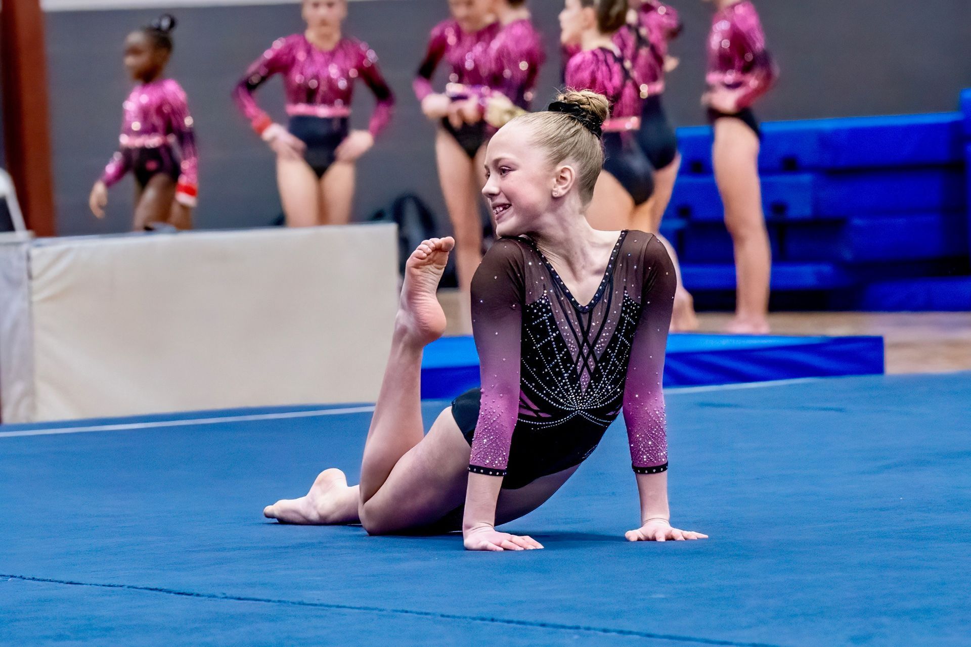 A female gymnast is sitting on the floor with her legs crossed.