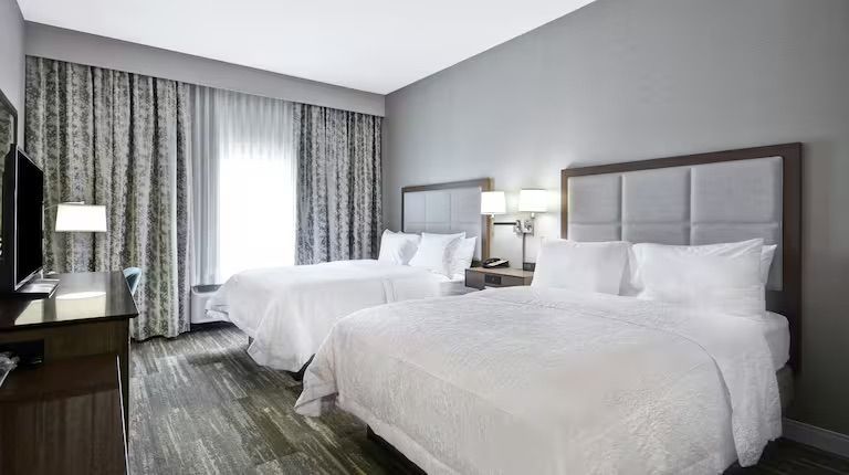 Hotel room with two queen beds, grey walls, and window with curtains.
