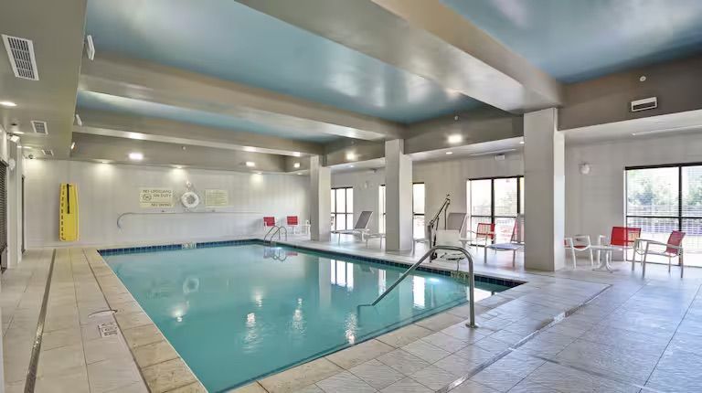 Indoor swimming pool with blue water, cream tile, and lounge chairs.