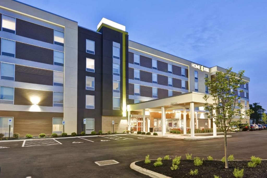 Modern hotel exterior at dusk with lit entrance and parking lot.