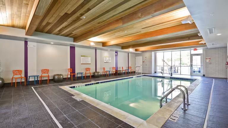 Indoor pool with gray tile, wooden beams, and orange chairs.