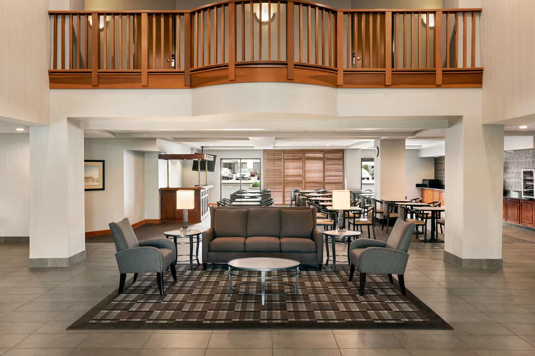 A hotel lobby with a couch , chairs , tables and a balcony.