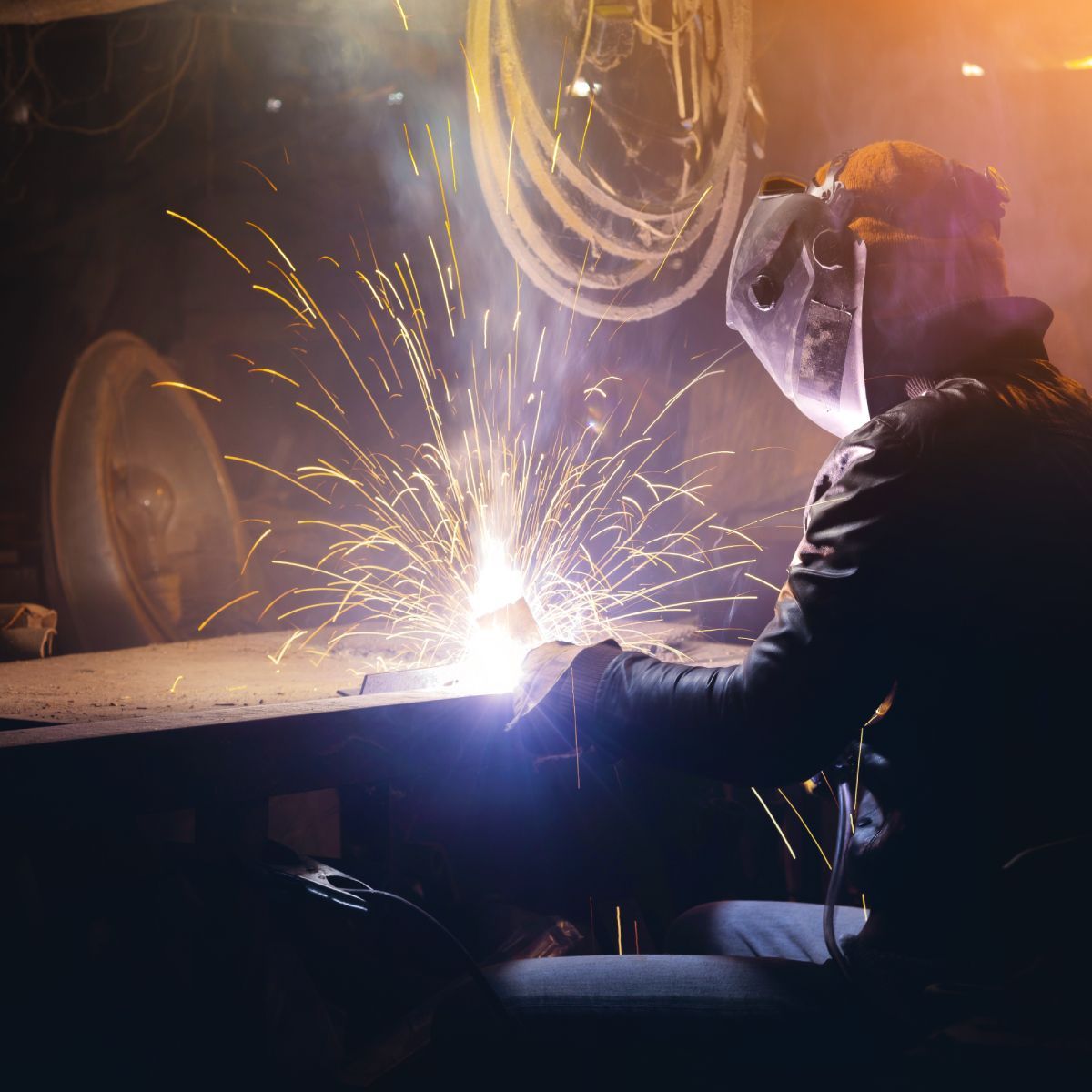 A man is welding a piece of metal in a dark room