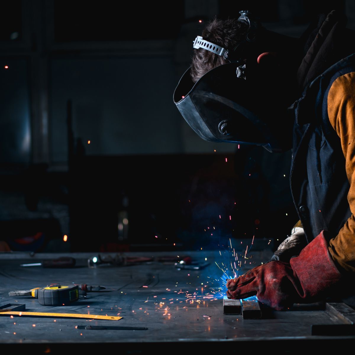 A man wearing a welding mask is welding a piece of metal.
