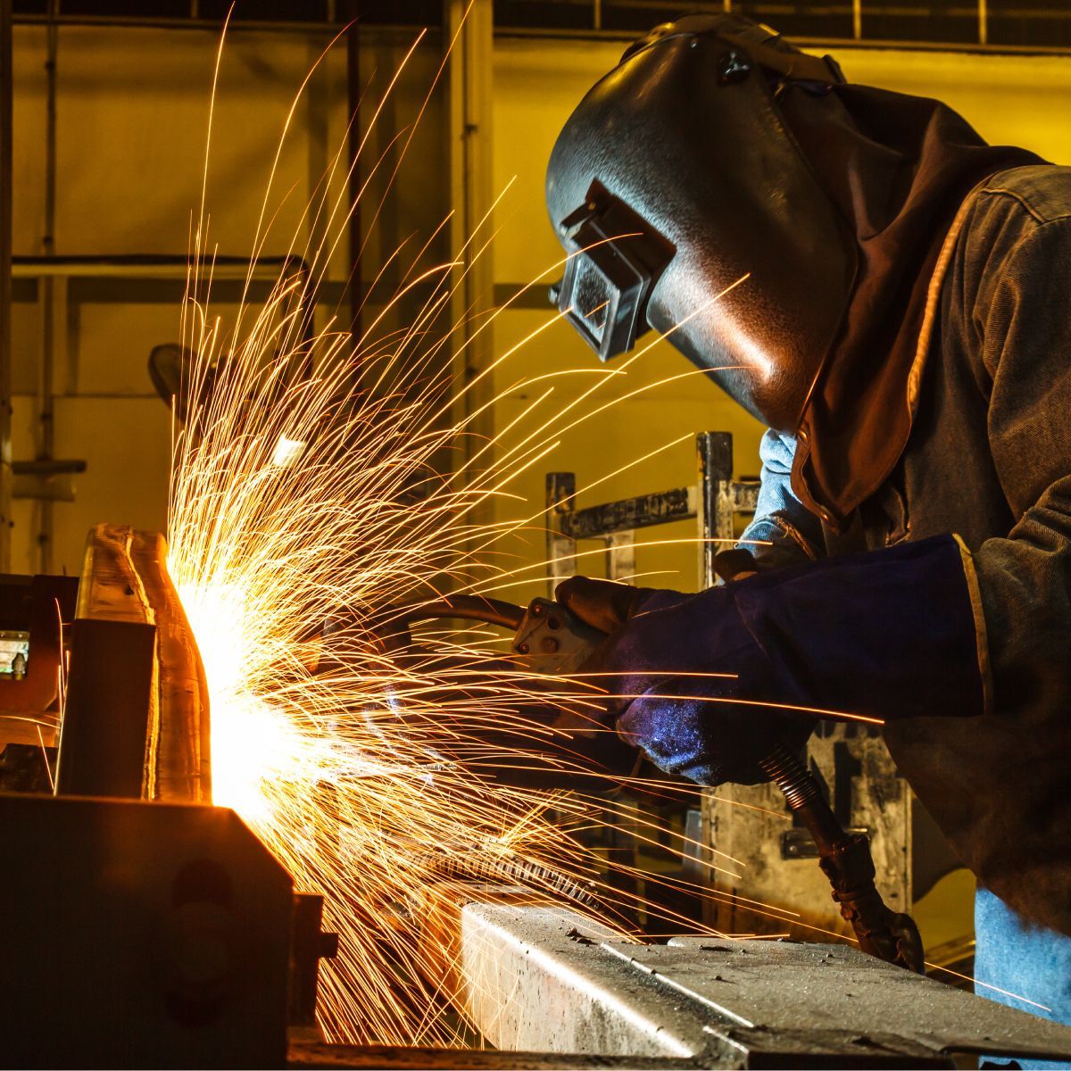A man wearing a welding helmet is welding a piece of metal