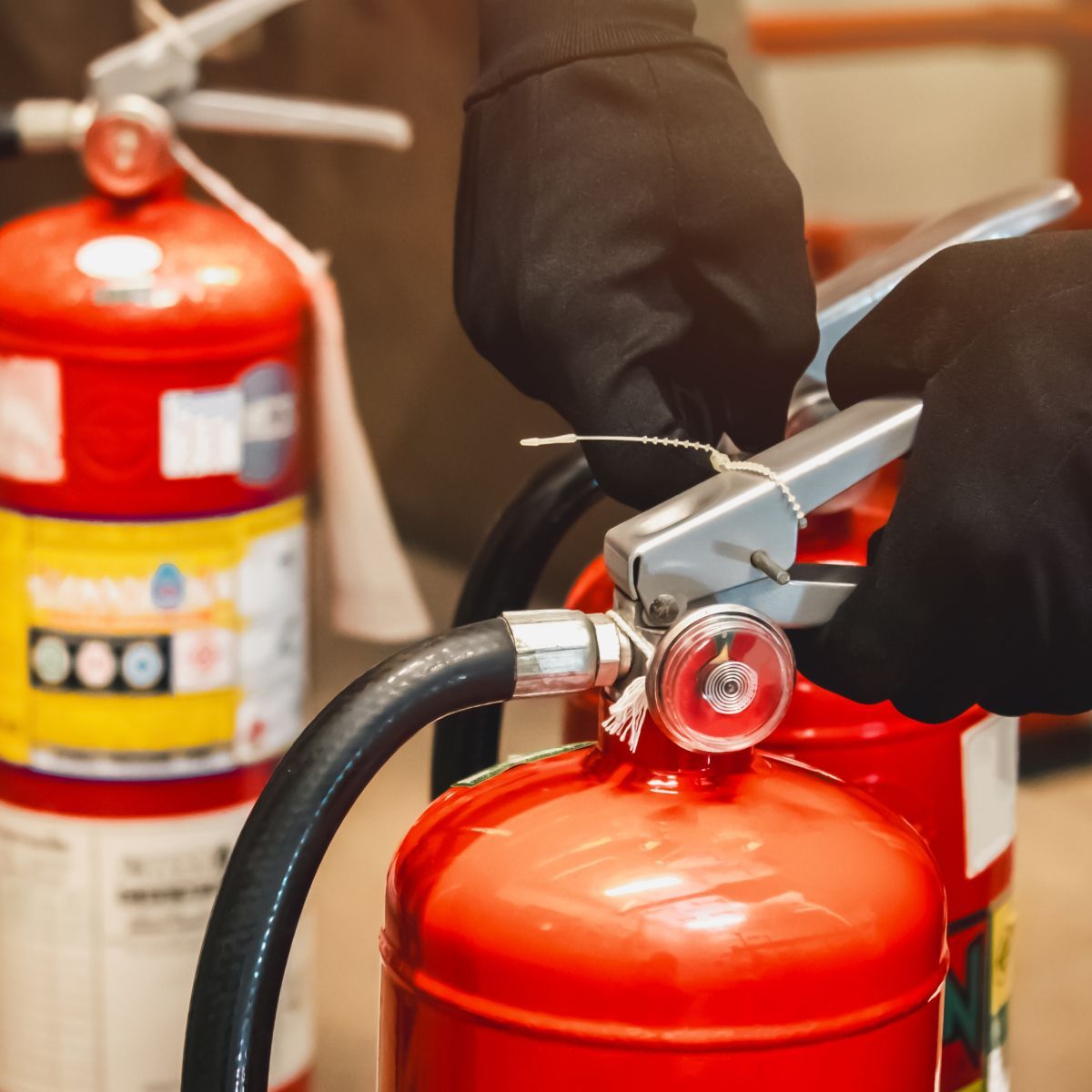 A person wearing black gloves is holding a red fire extinguisher