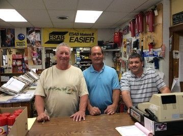 Three men are standing in front of a counter in a store.