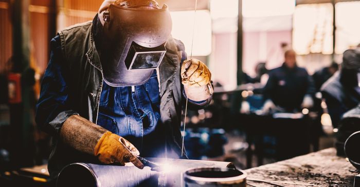 A man wearing a welding mask is welding a piece of metal