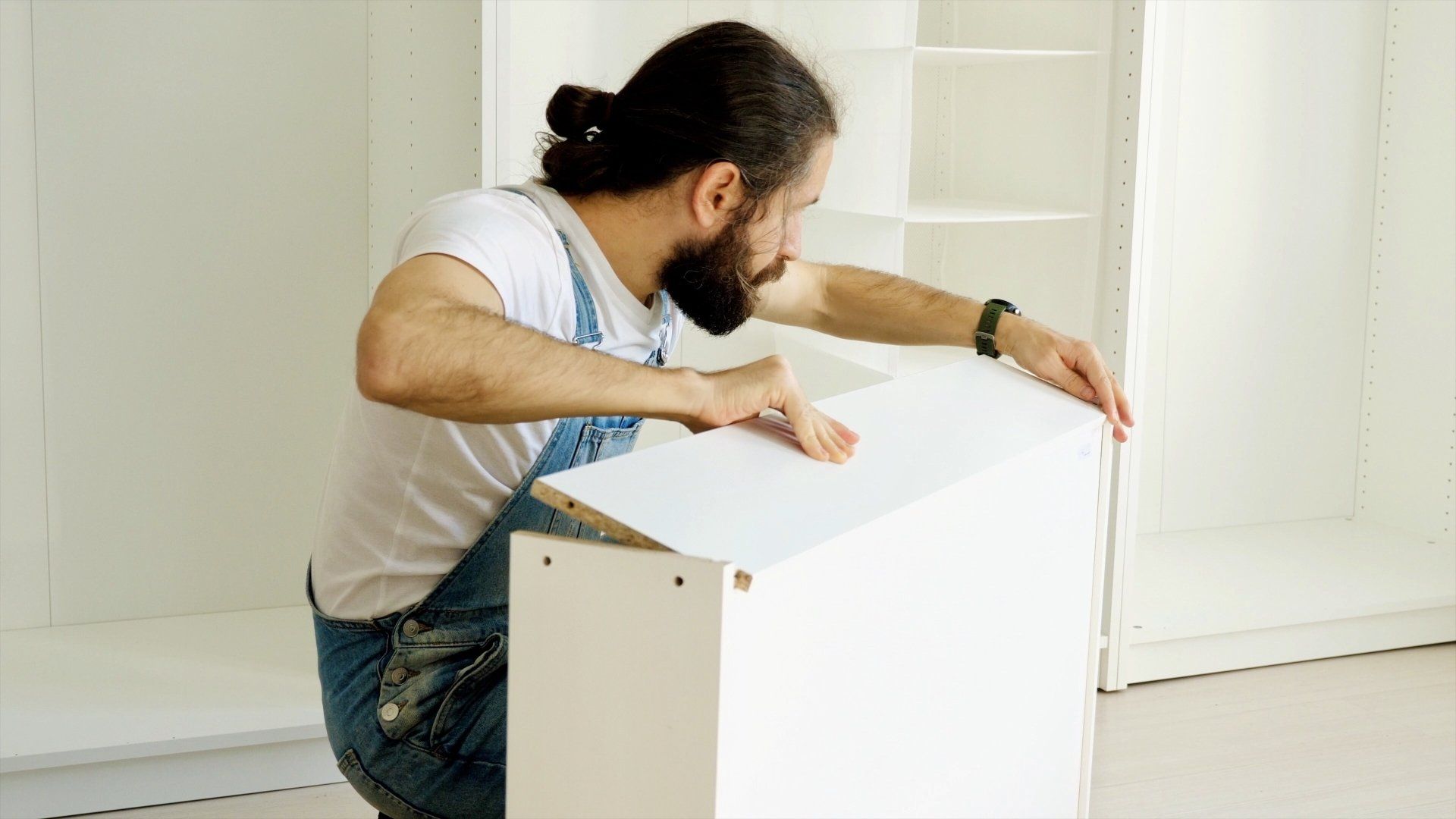 Homme assemblant une armoire blanche ; décor intérieur, expression concentrée.