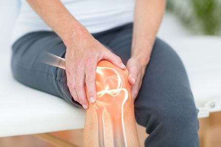 Person holding a glowing painful knee while seated on a couch