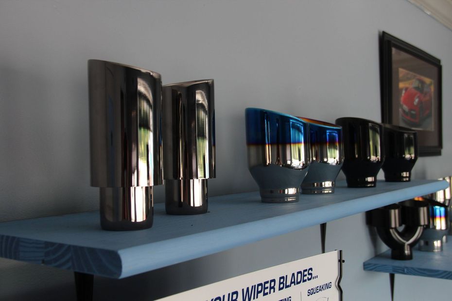 A row of shiny metal exhaust tips displayed on a blue shelf.