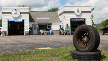 Auto repair shop with open bays and a tire display in front under a partly cloudy sky