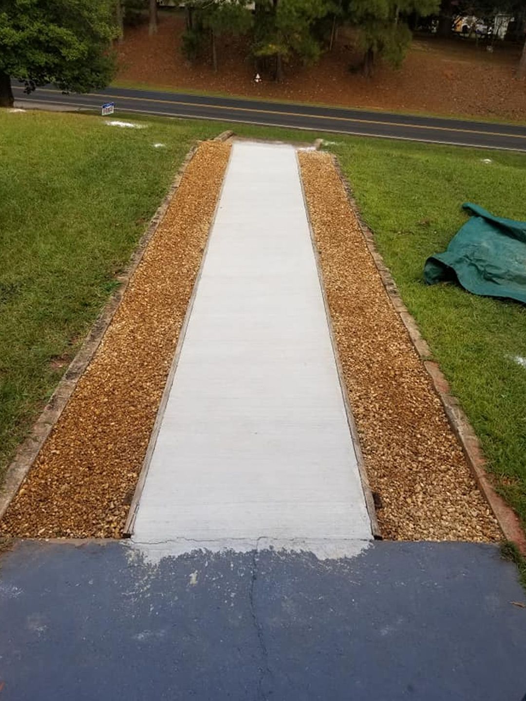 A freshly poured concrete sidewalk centered between two strips of mulch, leading toward a road in a grassy yard.