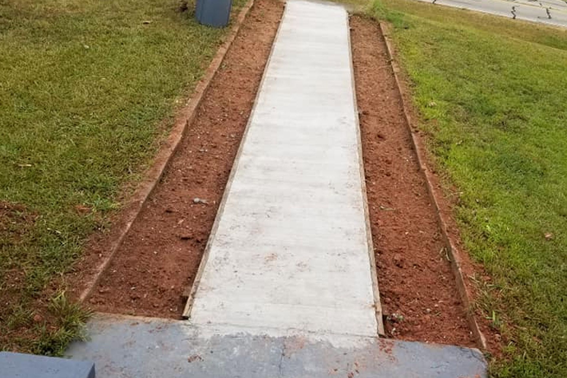 A newly poured concrete walkway set between two strips of exposed soil, bordered by grass.
