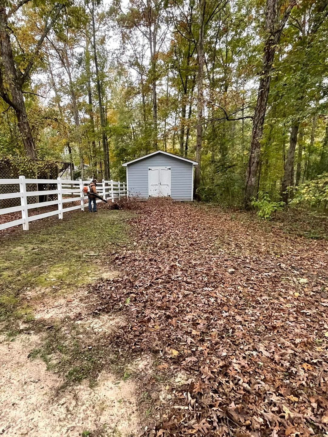 A blue house with a white garage sits at the end of a long concrete driveway, with a lawnmower parked on the side.