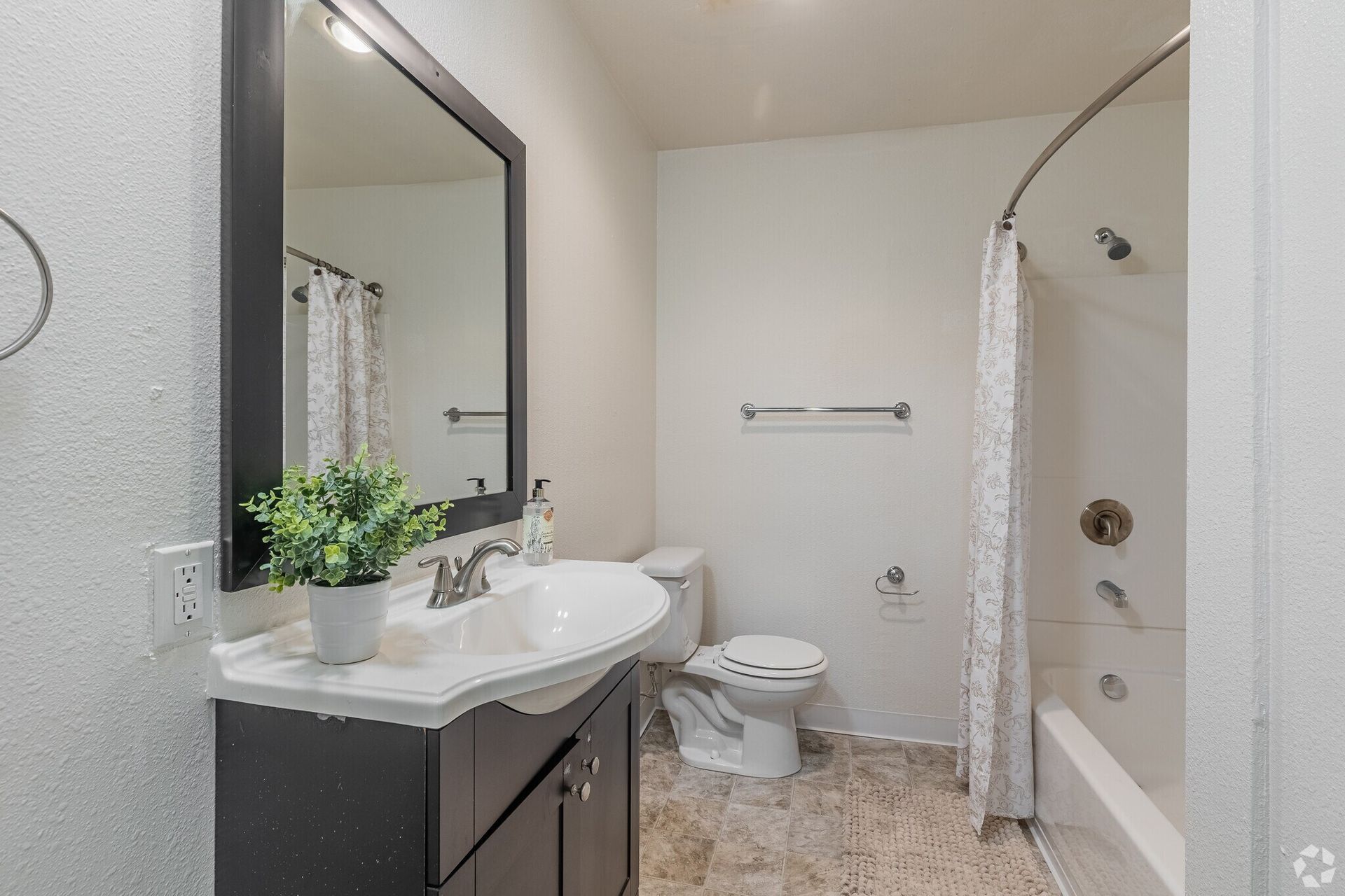 Compact bathroom with vanity, large mirror, toilet, and shower curtain in a light-colored interior.