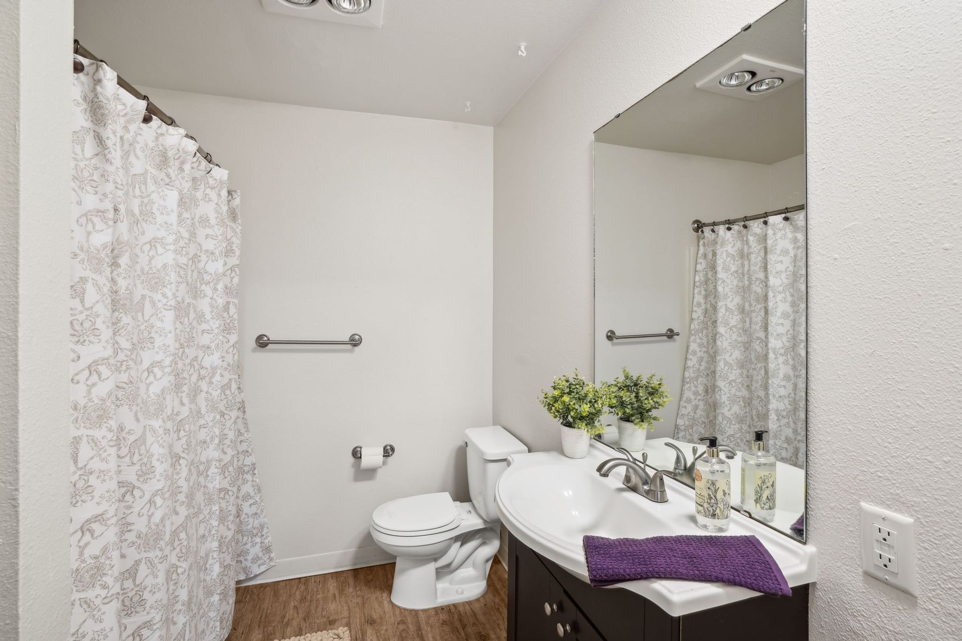 Bright bathroom with toilet, vanity sink, mirror, shower curtain, and purple towel.