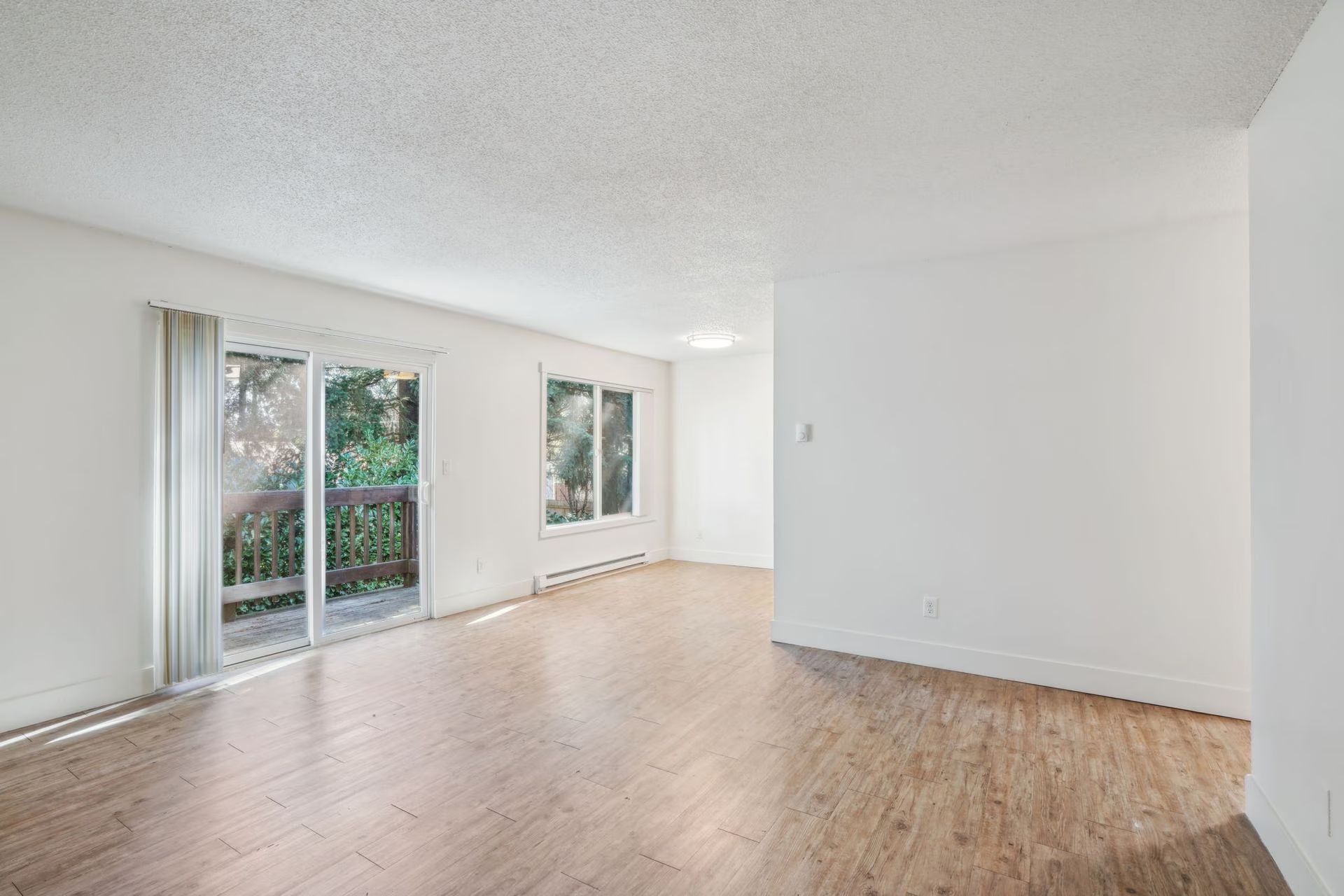 Bright empty living room with hardwood floors, white walls, and sliding glass doors to a patio.