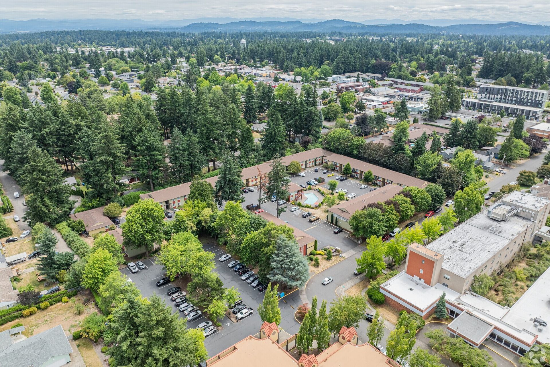 Aerial view of a tree-filled campus with buildings, parking lots, and distant city skyline
