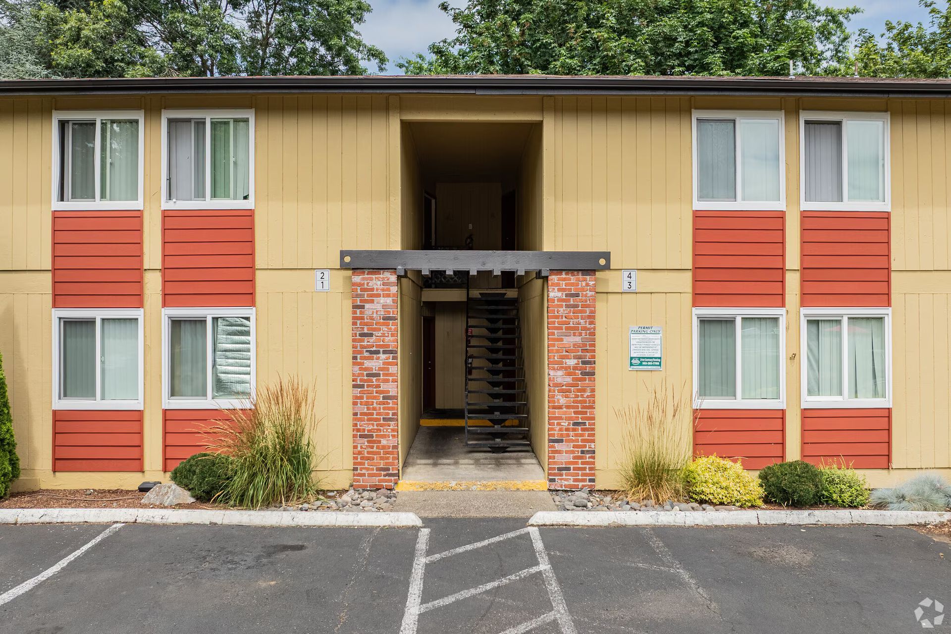Two-story apartment building with tan and orange siding and a central covered entrance