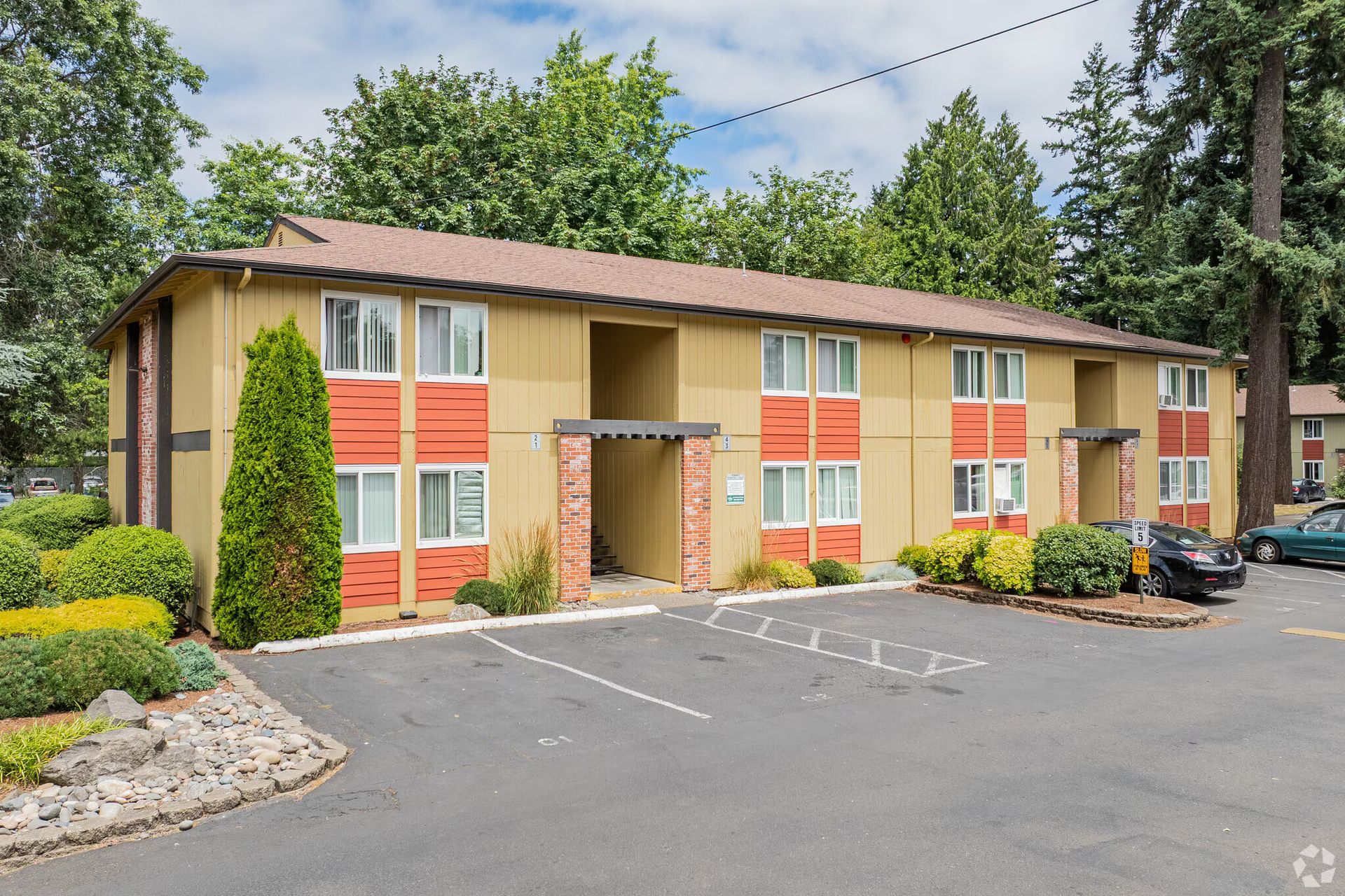 Apartment building exterior with beige siding, orange shutters, and a parking lot in front