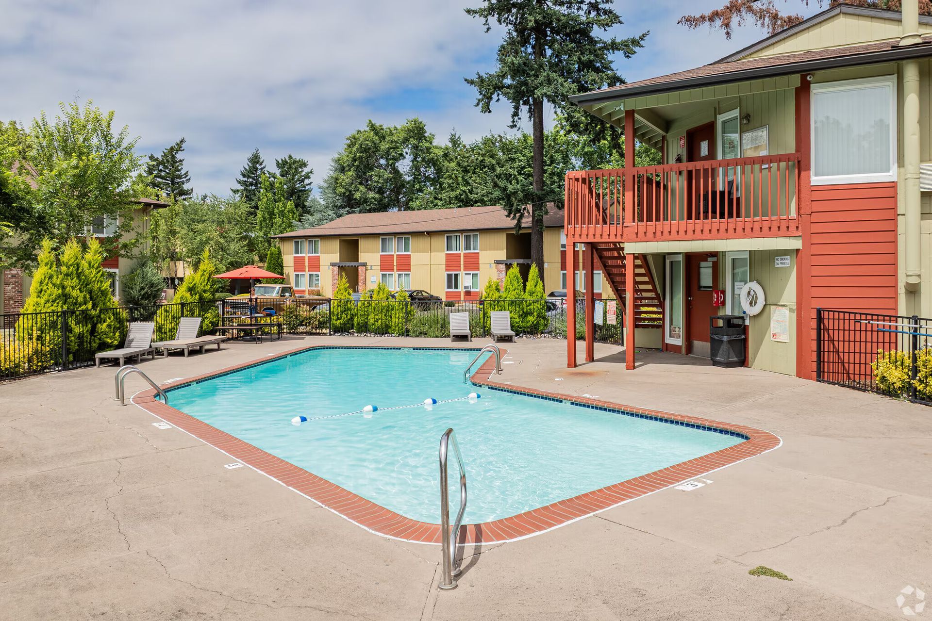 Apartment complex pool with turquoise water and a red balcony under sunny skies