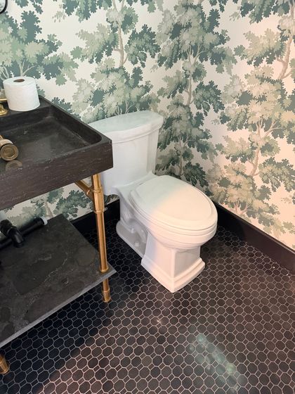 Bathroom with a white toilet beside a dark vanity, floral wallpaper, and patterned black floor tiles.