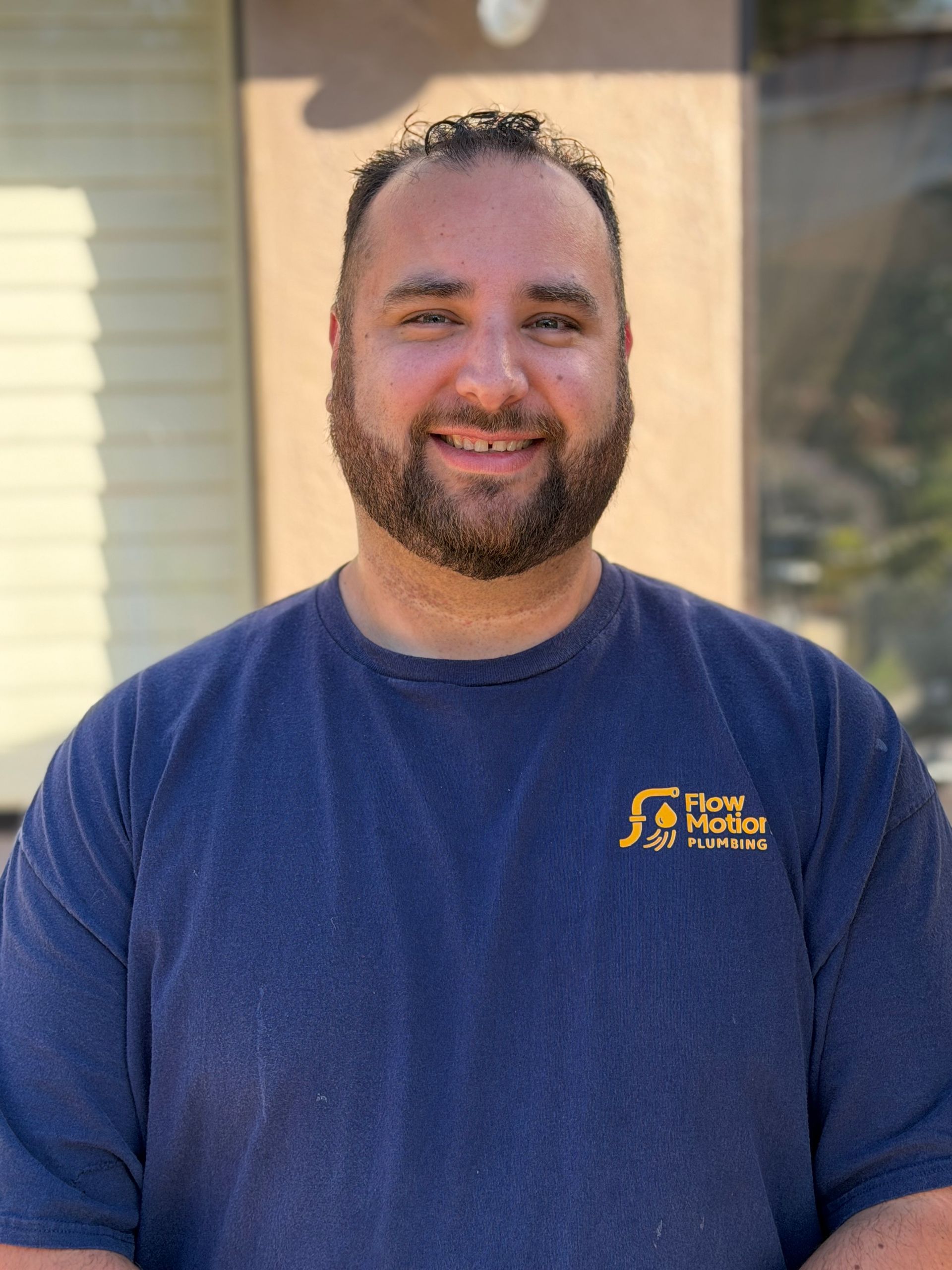 Smiling man in a blue shirt standing outdoors in front of a house.