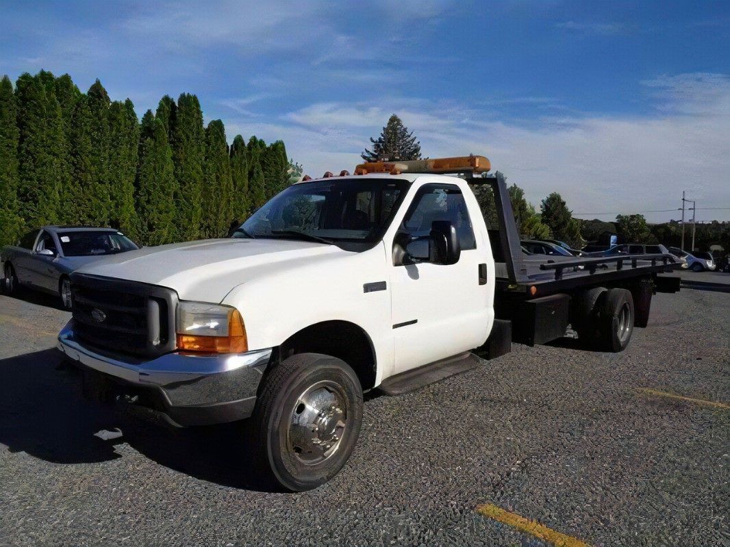 A white tow truck is parked in a gravel lot.